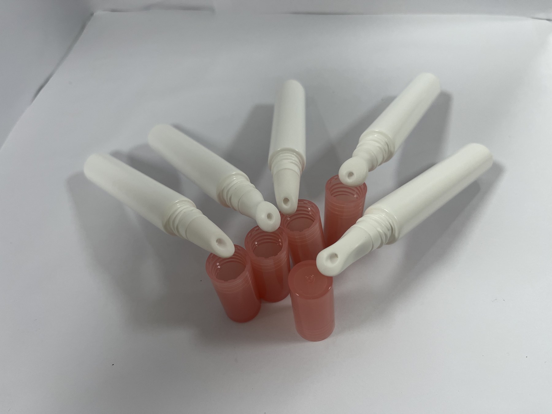 A selection of different cosmetic tube applicator tips with coral-colored caps