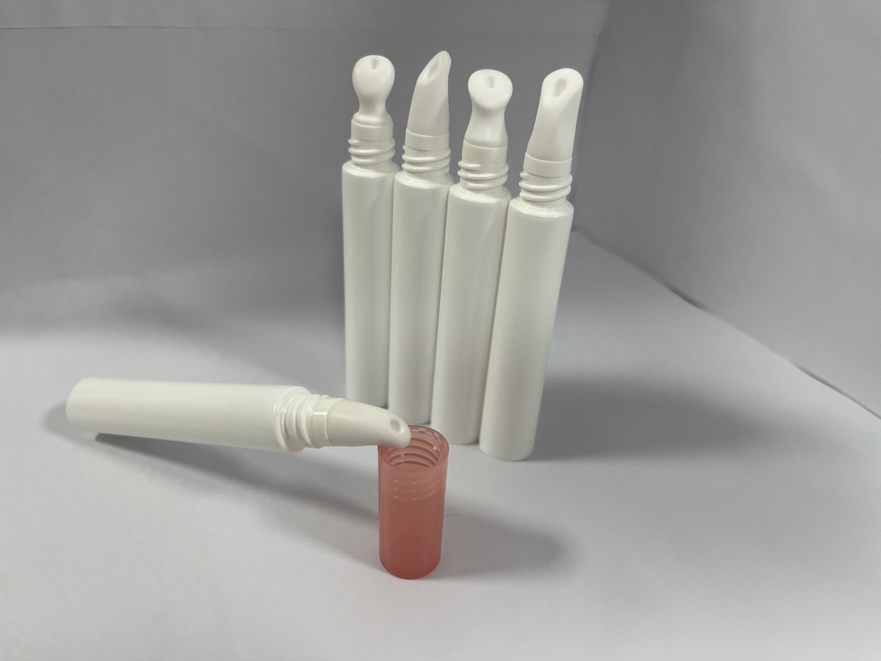 White cosmetic tubes with different applicator tips and translucent coral caps